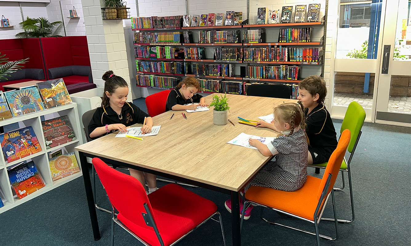 students sit in the school library colouring in worksheets